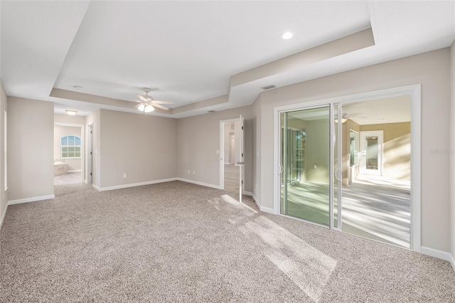 carpeted spare room featuring a tray ceiling and ceiling fan