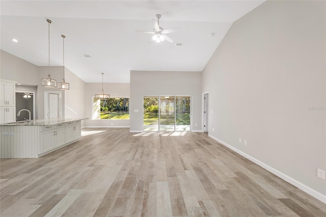 unfurnished living room with ceiling fan, light wood-type flooring, sink, and high vaulted ceiling