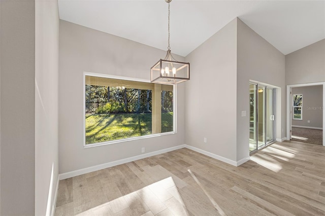 unfurnished dining area featuring light hardwood / wood-style flooring, high vaulted ceiling, and a chandelier