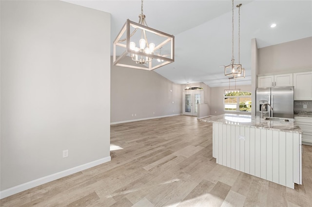 kitchen featuring white cabinetry, hanging light fixtures, stainless steel fridge, an island with sink, and light hardwood / wood-style floors