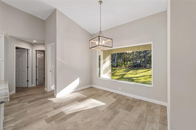 unfurnished dining area featuring light hardwood / wood-style flooring, high vaulted ceiling, and a notable chandelier