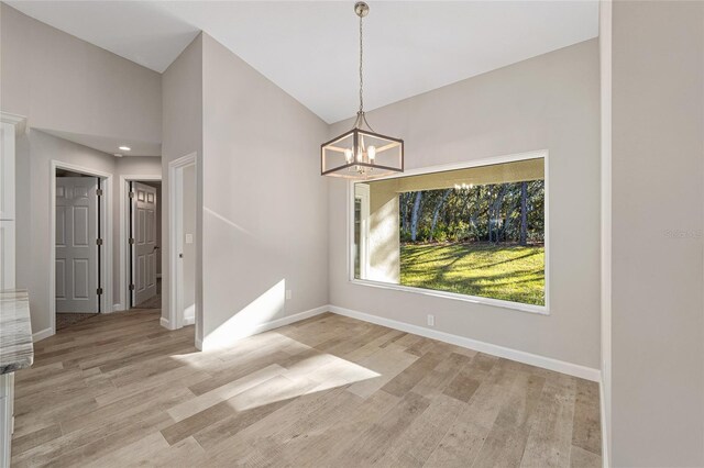 unfurnished dining area featuring light hardwood / wood-style flooring, high vaulted ceiling, and a notable chandelier