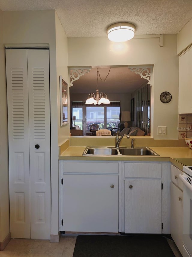 kitchen with white cabinets, a textured ceiling, a notable chandelier, and sink