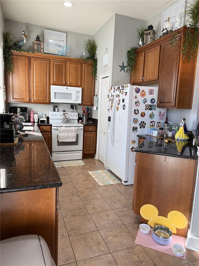 kitchen featuring white appliances, dark stone counters, and light tile patterned floors