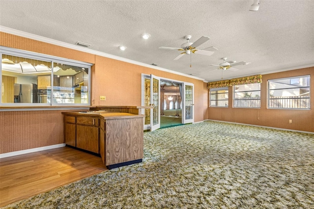 kitchen featuring wood-type flooring, a textured ceiling, stainless steel refrigerator, and ornamental molding