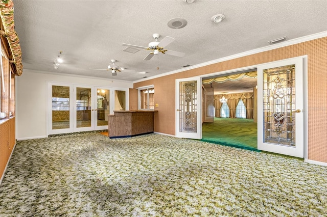 unfurnished living room with a wealth of natural light, french doors, crown molding, carpet floors, and a textured ceiling