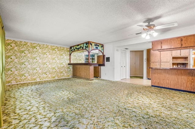 unfurnished living room featuring ceiling fan, light colored carpet, a textured ceiling, and ornamental molding