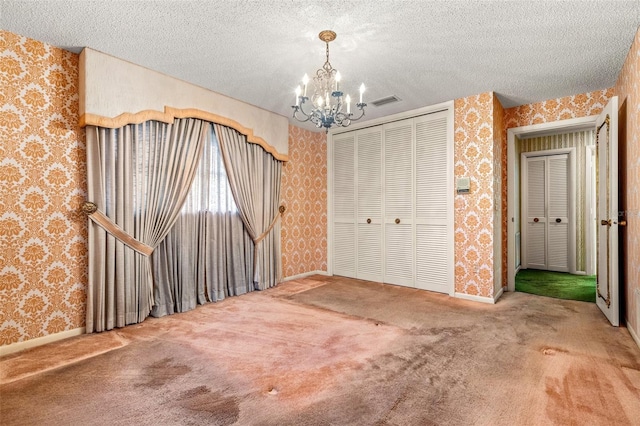 unfurnished bedroom with a closet, carpet floors, a textured ceiling, and a notable chandelier