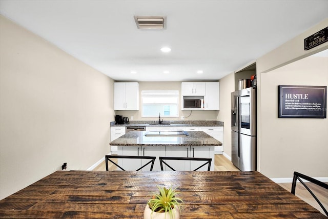 kitchen with sink, stainless steel appliances, dark stone countertops, a kitchen bar, and white cabinets