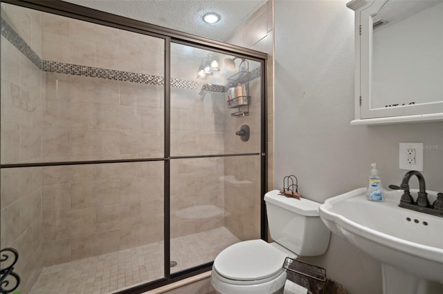 bathroom with toilet, sink, a shower with door, and a textured ceiling