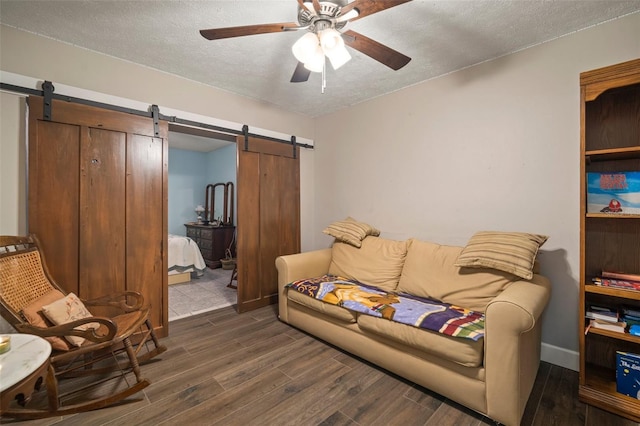 living room featuring a textured ceiling, a barn door, ceiling fan, and dark wood-type flooring