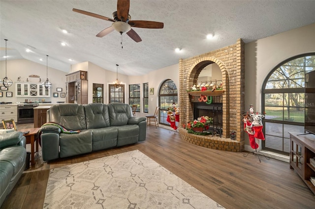 living room featuring ceiling fan, dark hardwood / wood-style flooring, a textured ceiling, vaulted ceiling, and a fireplace