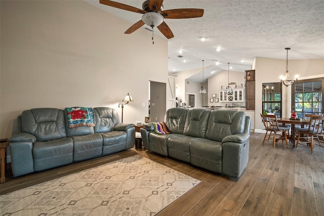 living room with a textured ceiling, ceiling fan with notable chandelier, dark hardwood / wood-style floors, and high vaulted ceiling