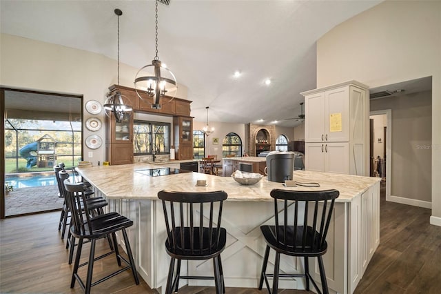 kitchen with dark wood-type flooring, pendant lighting, lofted ceiling, a kitchen bar, and white cabinets