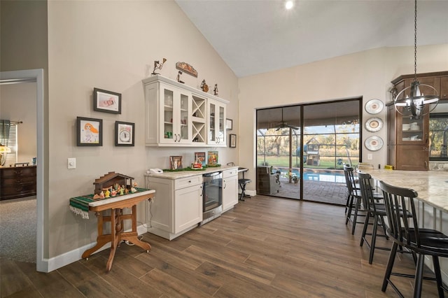 kitchen with light stone countertops, high vaulted ceiling, white cabinets, dark hardwood / wood-style floors, and hanging light fixtures