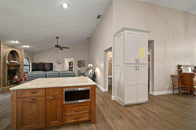 kitchen with a fireplace, ceiling fan, dark wood-type flooring, white cabinets, and a kitchen island