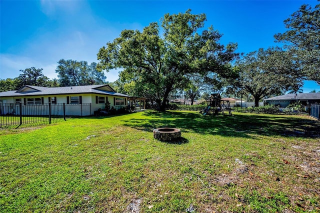 view of yard with a fenced backyard, a fire pit, and a playground