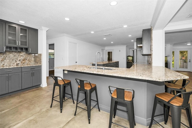 kitchen with gray cabinets, decorative backsplash, glass insert cabinets, a peninsula, and a kitchen breakfast bar