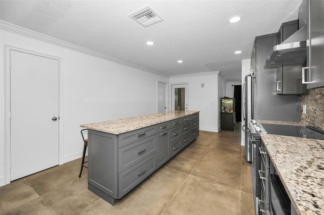 kitchen featuring visible vents, a kitchen island, light stone counters, a kitchen breakfast bar, and stainless steel stove