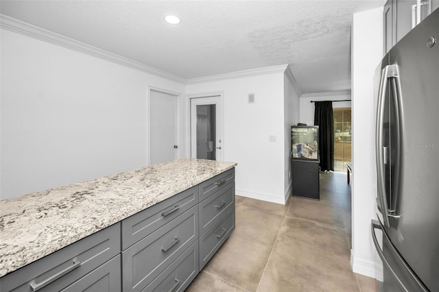 kitchen featuring baseboards, ornamental molding, gray cabinets, freestanding refrigerator, and light stone countertops