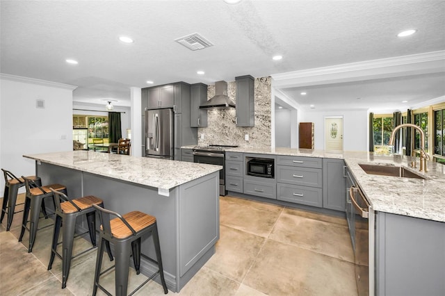 kitchen featuring appliances with stainless steel finishes, a breakfast bar area, wall chimney range hood, and gray cabinetry