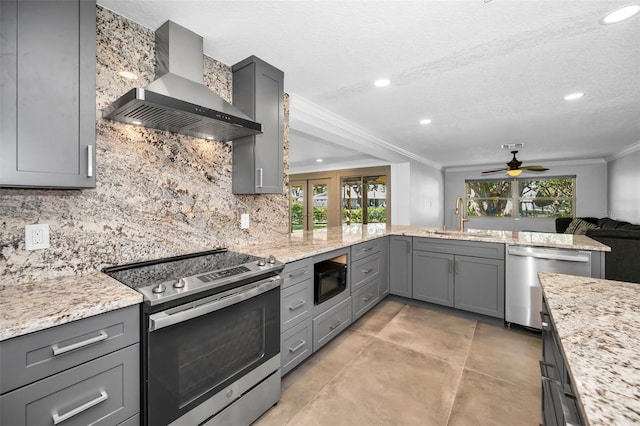 kitchen with crown molding, gray cabinets, appliances with stainless steel finishes, a sink, and wall chimney exhaust hood