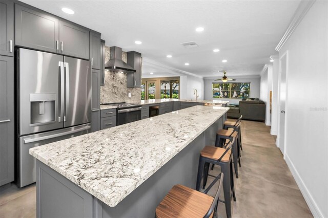 kitchen with wall chimney exhaust hood, appliances with stainless steel finishes, a kitchen breakfast bar, open floor plan, and a peninsula