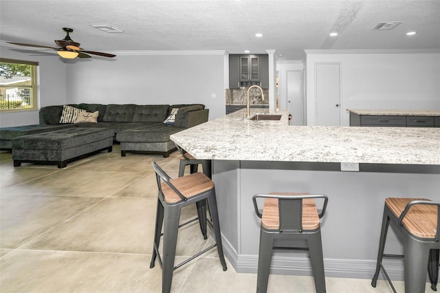 kitchen with a breakfast bar area, visible vents, gray cabinetry, glass insert cabinets, and a sink