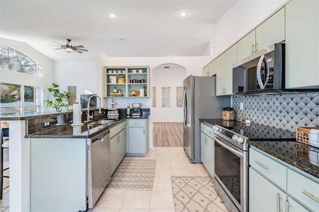 kitchen featuring sink, ceiling fan, dark stone countertops, light tile patterned flooring, and stainless steel appliances