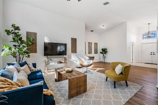 living room with visible vents, wood finished floors, high vaulted ceiling, and an inviting chandelier