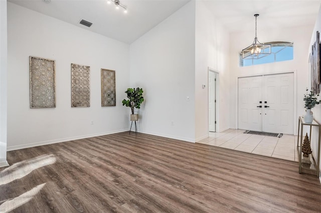foyer entrance featuring a notable chandelier, high vaulted ceiling, baseboards, wood finished floors, and visible vents