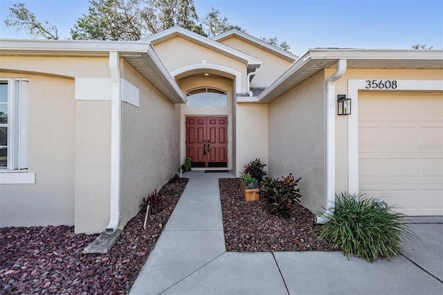 entrance to property featuring an attached garage and stucco siding