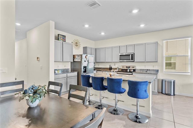 kitchen featuring light stone counters, appliances with stainless steel finishes, a center island with sink, and light tile patterned floors