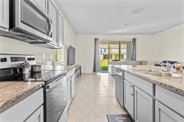 kitchen featuring sink, light tile patterned floors, appliances with stainless steel finishes, plenty of natural light, and light stone counters