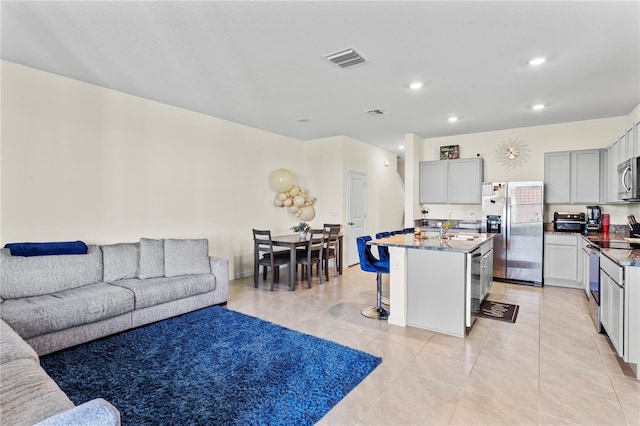 kitchen featuring gray cabinets, a kitchen island with sink, a kitchen bar, stainless steel appliances, and light tile patterned flooring