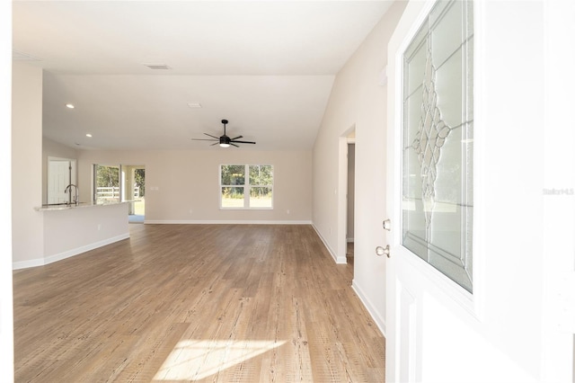 unfurnished living room with ceiling fan, sink, light hardwood / wood-style floors, and vaulted ceiling