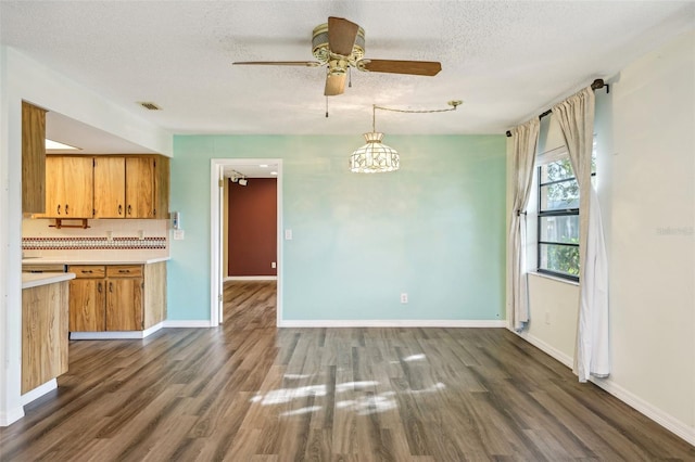 unfurnished dining area featuring a textured ceiling, ceiling fan with notable chandelier, and dark wood-type flooring