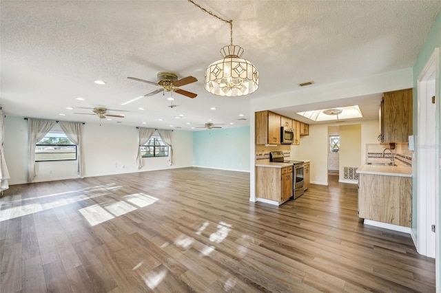 unfurnished living room featuring a textured ceiling, hardwood / wood-style floors, ceiling fan with notable chandelier, and sink