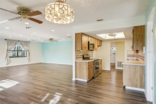 kitchen with sink, hanging light fixtures, stainless steel appliances, dark hardwood / wood-style floors, and ceiling fan with notable chandelier