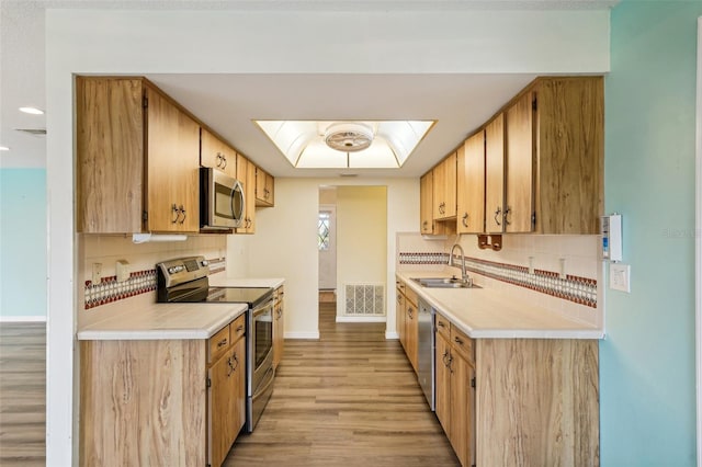 kitchen with tasteful backsplash, a skylight, stainless steel appliances, sink, and light hardwood / wood-style floors