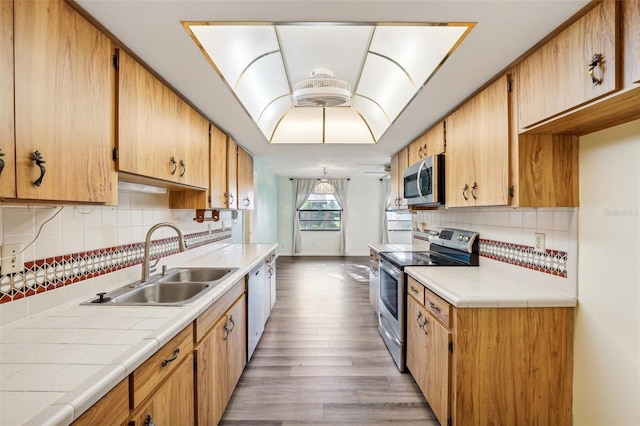 kitchen with appliances with stainless steel finishes, tasteful backsplash, sink, tile countertops, and hardwood / wood-style flooring