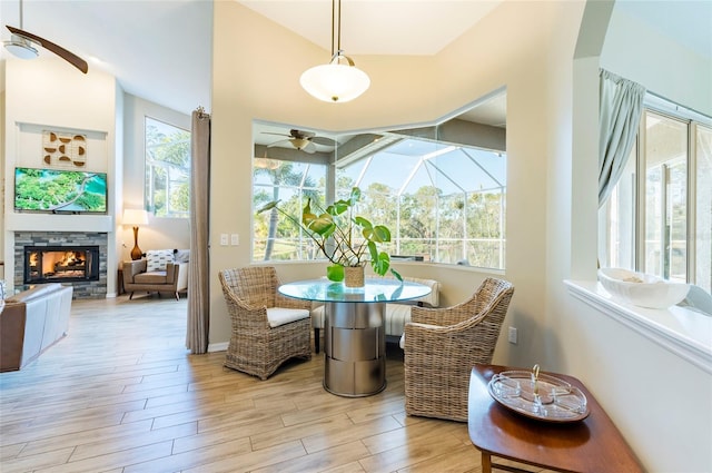 dining space with light hardwood / wood-style flooring, a wealth of natural light, a stone fireplace, and ceiling fan