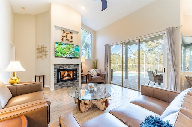 living room with a fireplace, light wood-type flooring, high vaulted ceiling, and ceiling fan