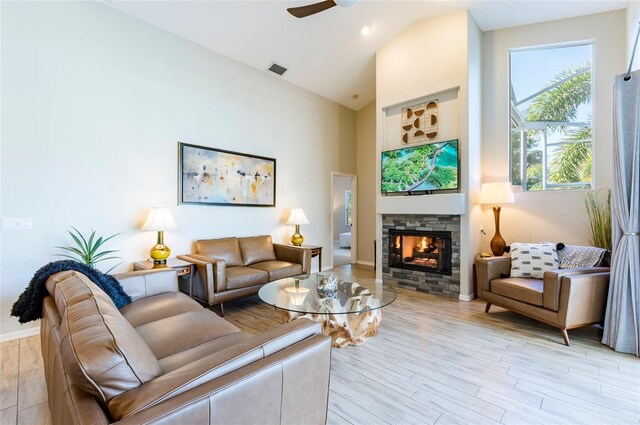 living room featuring light wood-type flooring, vaulted ceiling, ceiling fan, and a stone fireplace