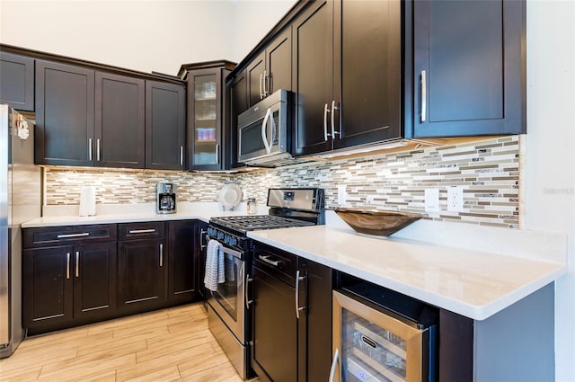 kitchen featuring decorative backsplash, light wood-type flooring, appliances with stainless steel finishes, dark brown cabinetry, and beverage cooler