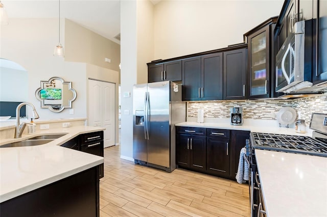 kitchen featuring sink, hanging light fixtures, stainless steel appliances, light hardwood / wood-style flooring, and high vaulted ceiling