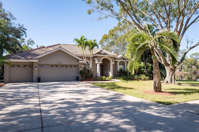 mediterranean / spanish home featuring a garage, a water view, and a front lawn