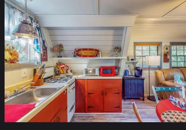 kitchen with gas range gas stove, sink, light hardwood / wood-style flooring, hanging light fixtures, and wood walls