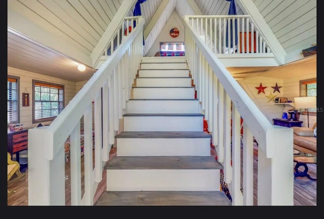 staircase with wood walls, wood-type flooring, high vaulted ceiling, and wooden ceiling