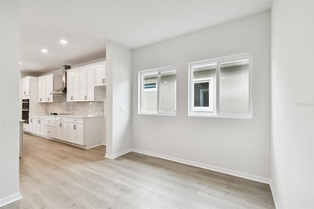 kitchen with white cabinets, light hardwood / wood-style floors, and wall chimney range hood